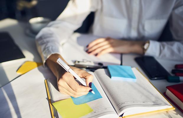 woman's manicured hands writing on sticky notes